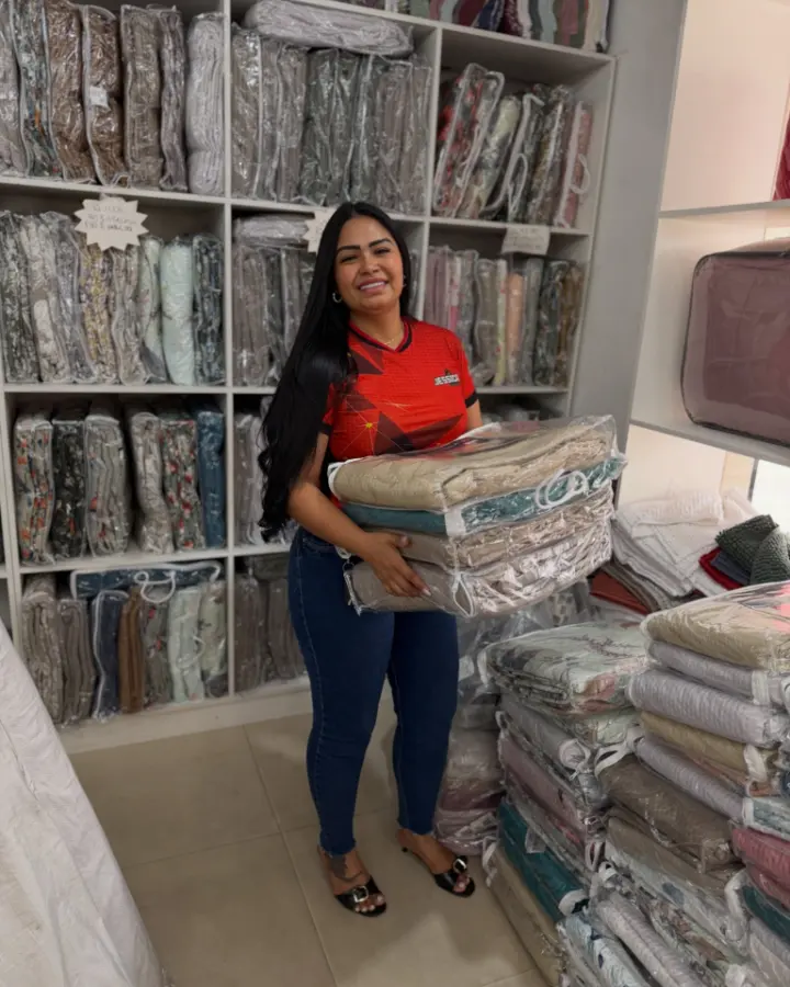 Jessica, dona da loja, segurando jogos de cama entre as prateleiras